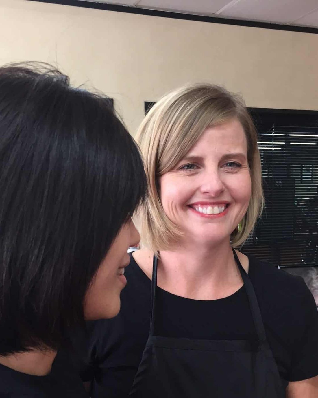 A stylist in a Baldwin apron smiles beside a client with a finished bob
