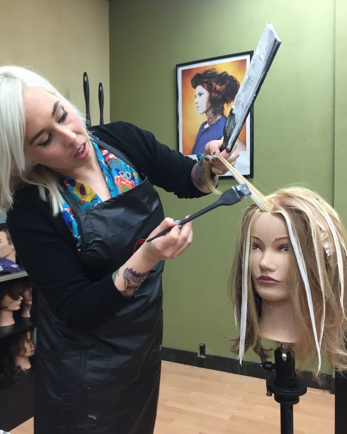 An instructor demonstrates a haircut on a mannequin while students watch