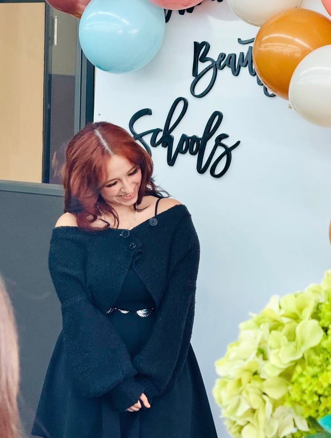 A graduate in front of the Beauty Schools balloon backdrop